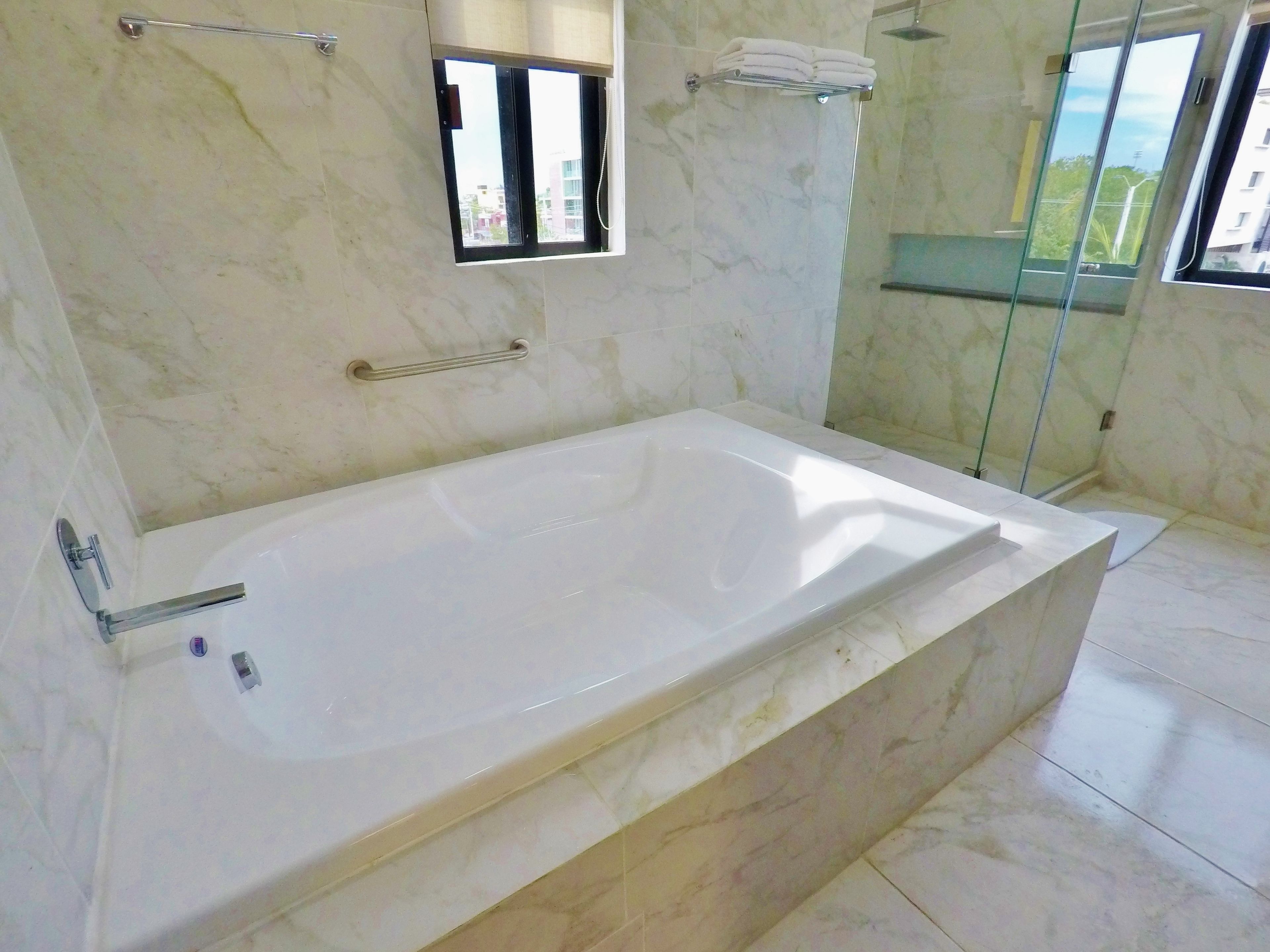Un baño moderno con una bañera grande, cabina de ducha con mampara de vidrio y ventana con vistas al exterior.