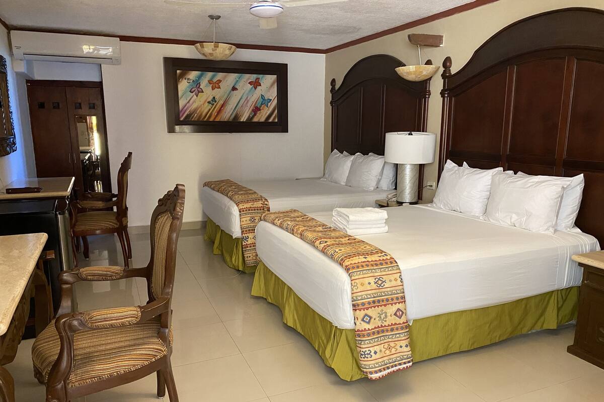 A hotel room with two beds, a dining area with chairs, a table, and a painting on the wall.