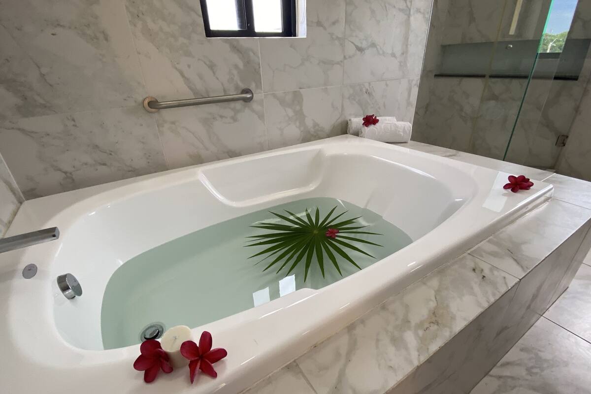 A modern bathroom with a large bathtub, marble tiles, a small window, and a handrail.