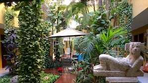 Un patio con un sendero de madera, una estatua de piedra y abundante vegetación.
