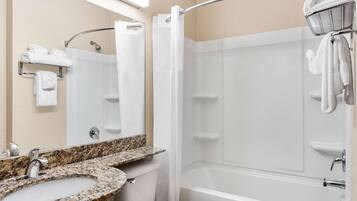 Une salle de bain moderne avec un lavabo surmonté d’un plan de travail en granit, des toilettes blanches, une baignoire et un rideau de douche.
