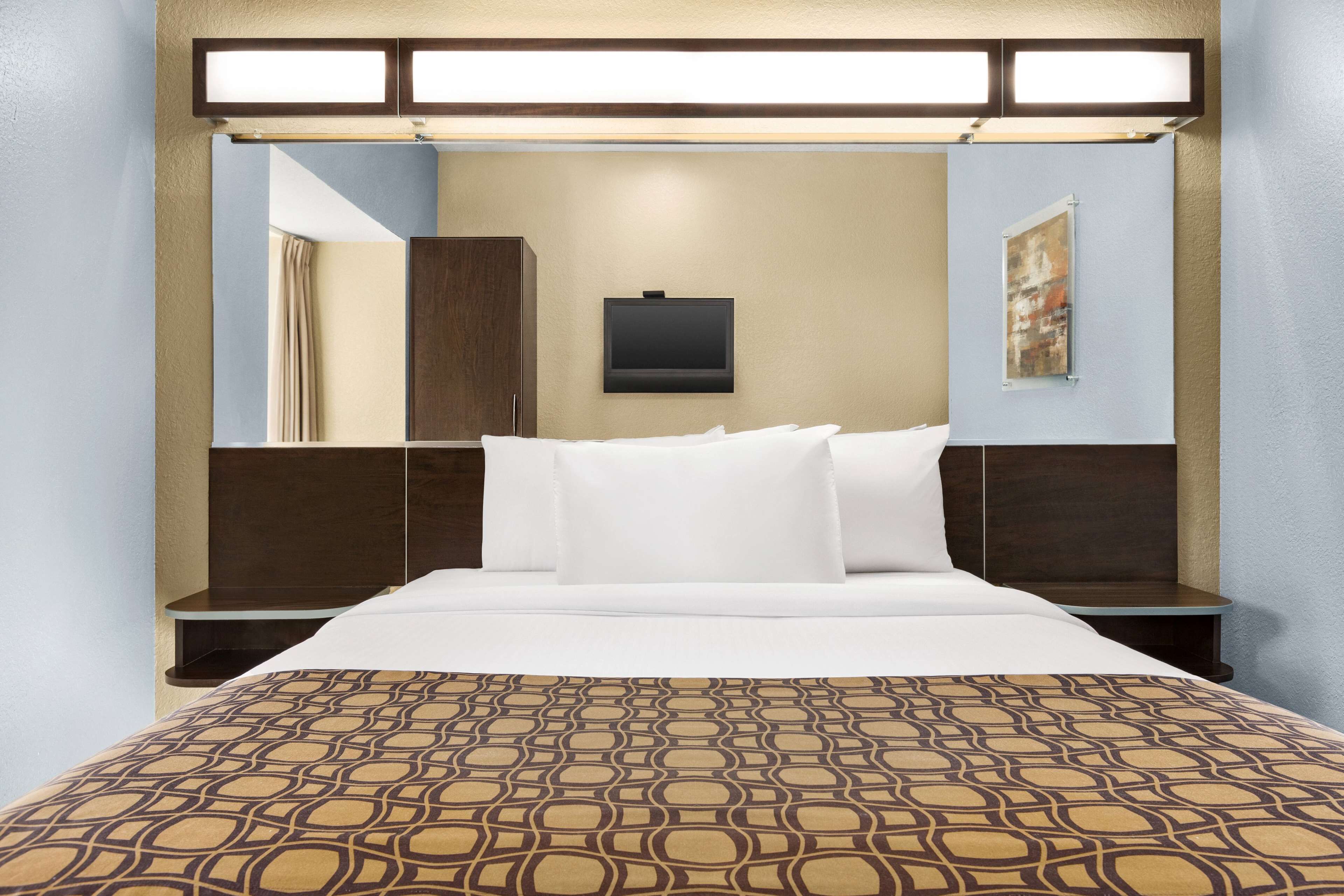 A hotel room with a large bed, a flat-screen TV mounted on the wall, and a patterned bedspread.