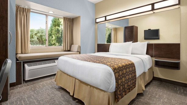 Een hotelkamer met een groot bed, een raam met gordijnen, een ingebouwde verwarming, een flatscreen televisie en een klein plankje.