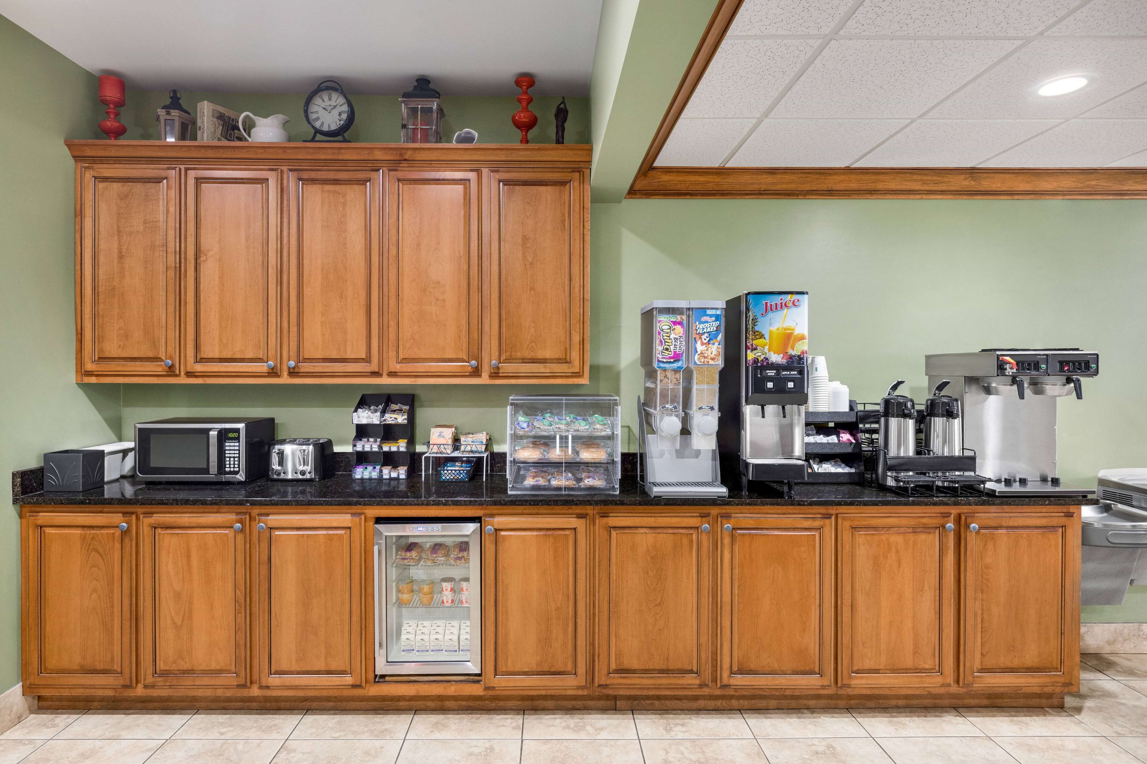 A kitchen with wooden cabinets, a microwave, a coffee machine, and a refrigerated display.