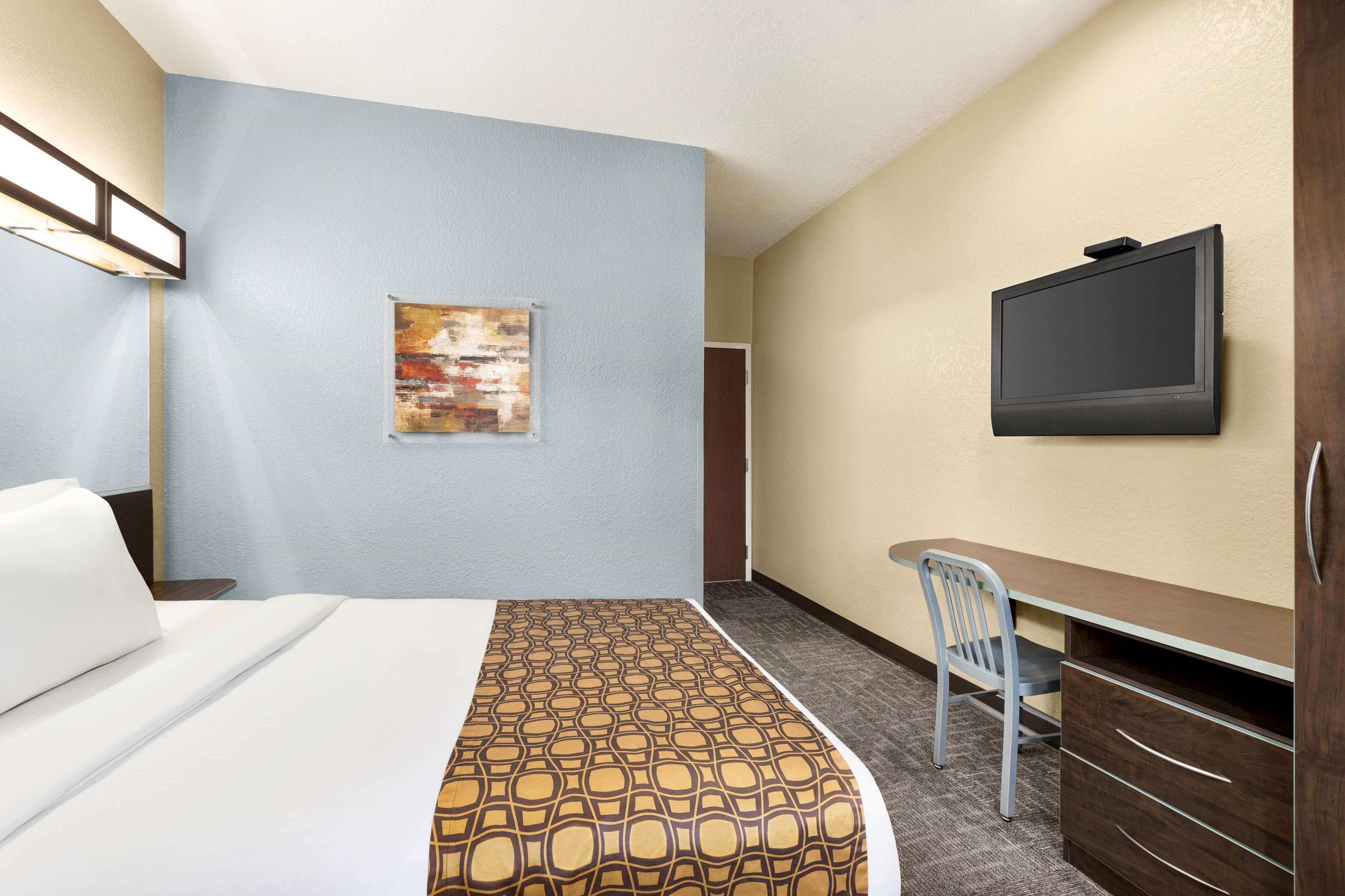 Habitación de hotel con cama, escritorio con silla, televisor y un cuadro en la pared.