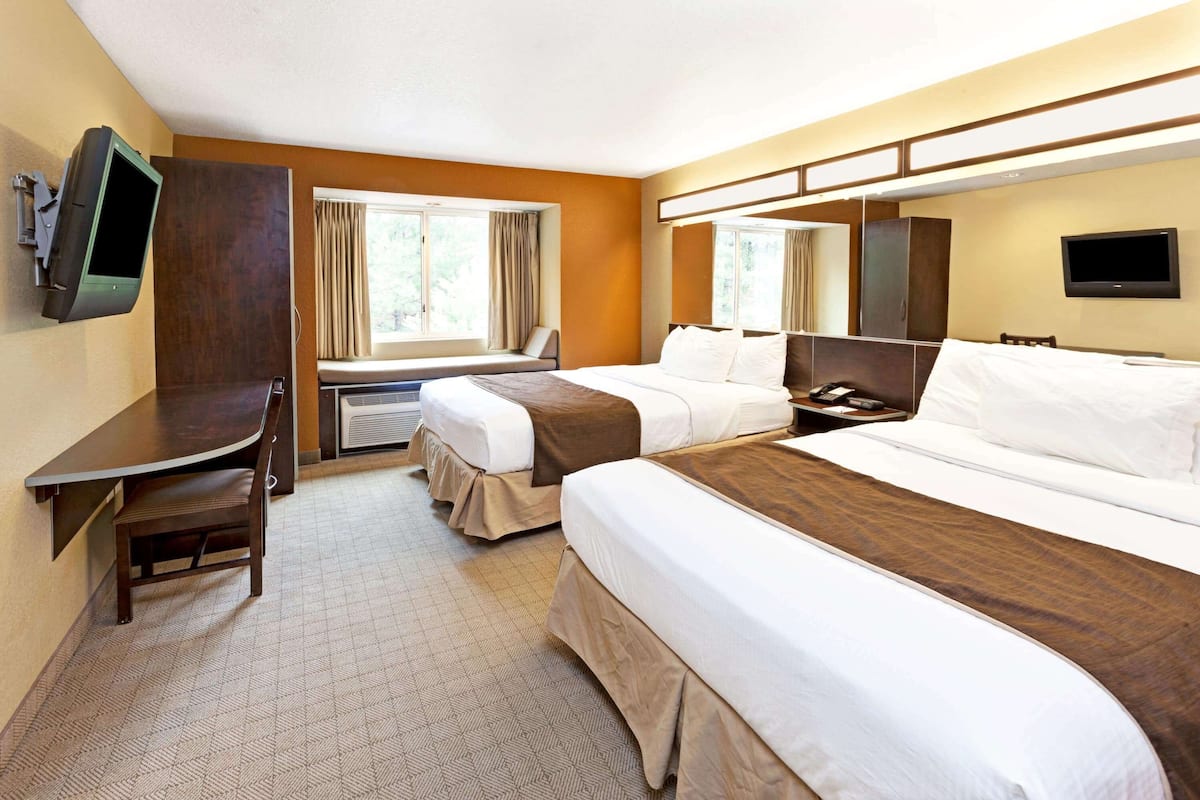 Une chambre d’hôtel avec deux lits, un bureau, une chaise, une télévision et une fenêtre avec des rideaux.