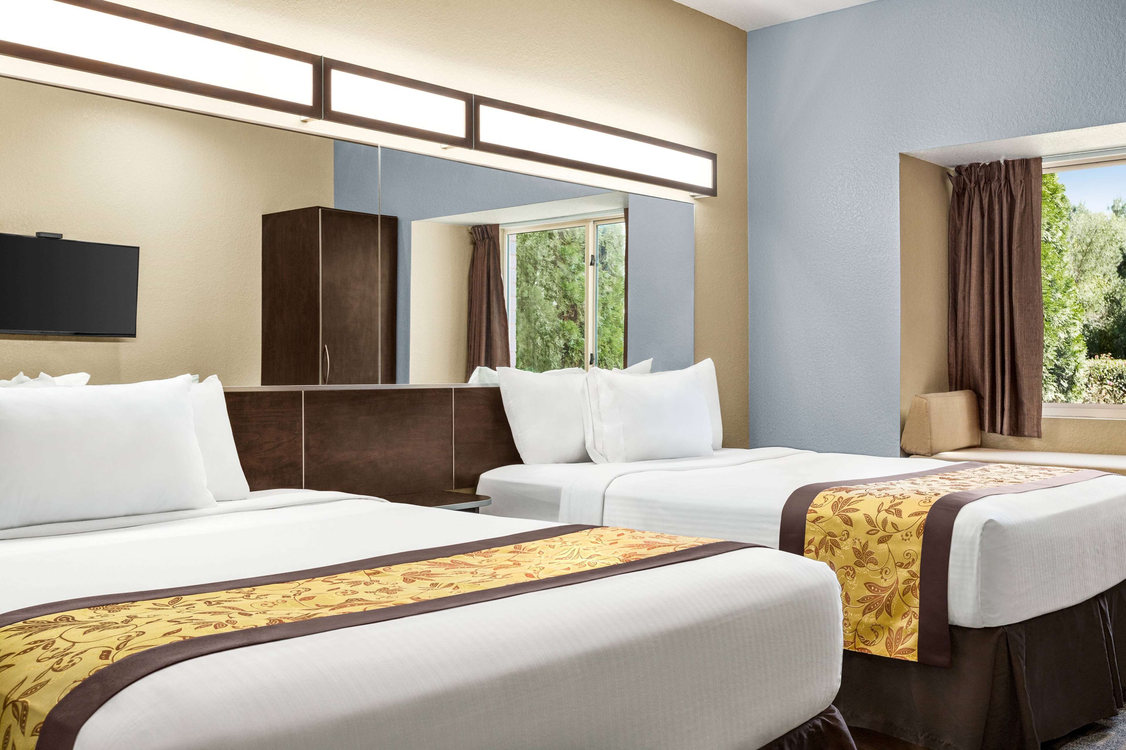 Habitación de hotel con dos camas, televisión de pantalla plana, armario y ventana con cortinas.