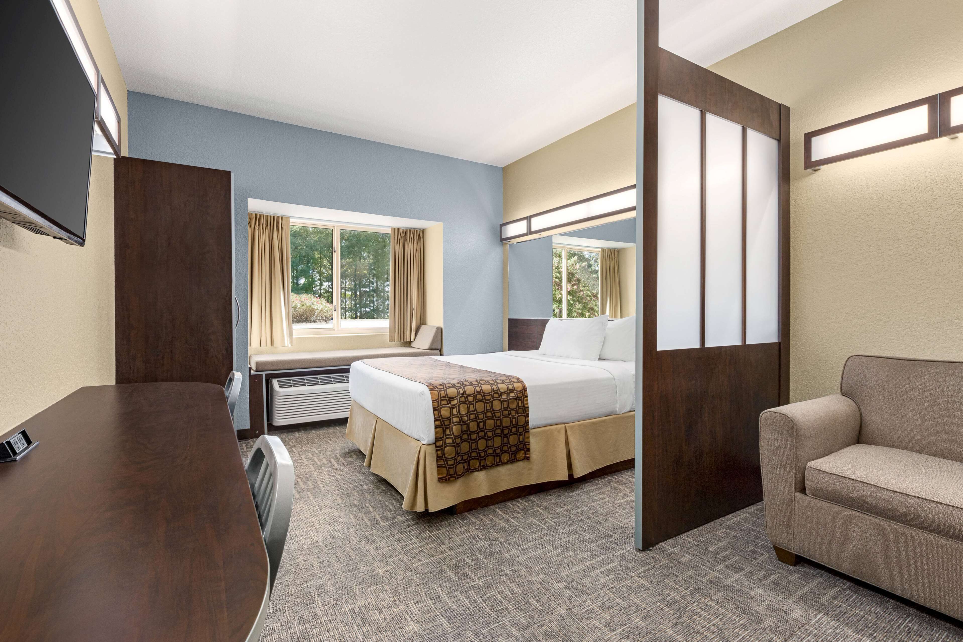 Habitación de hotel con cama, escritorio, silla, televisor y ventana con cortinas.