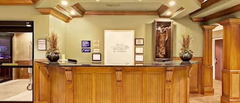 A reception desk with a wooden finish, framed certificates, and two potted plants.