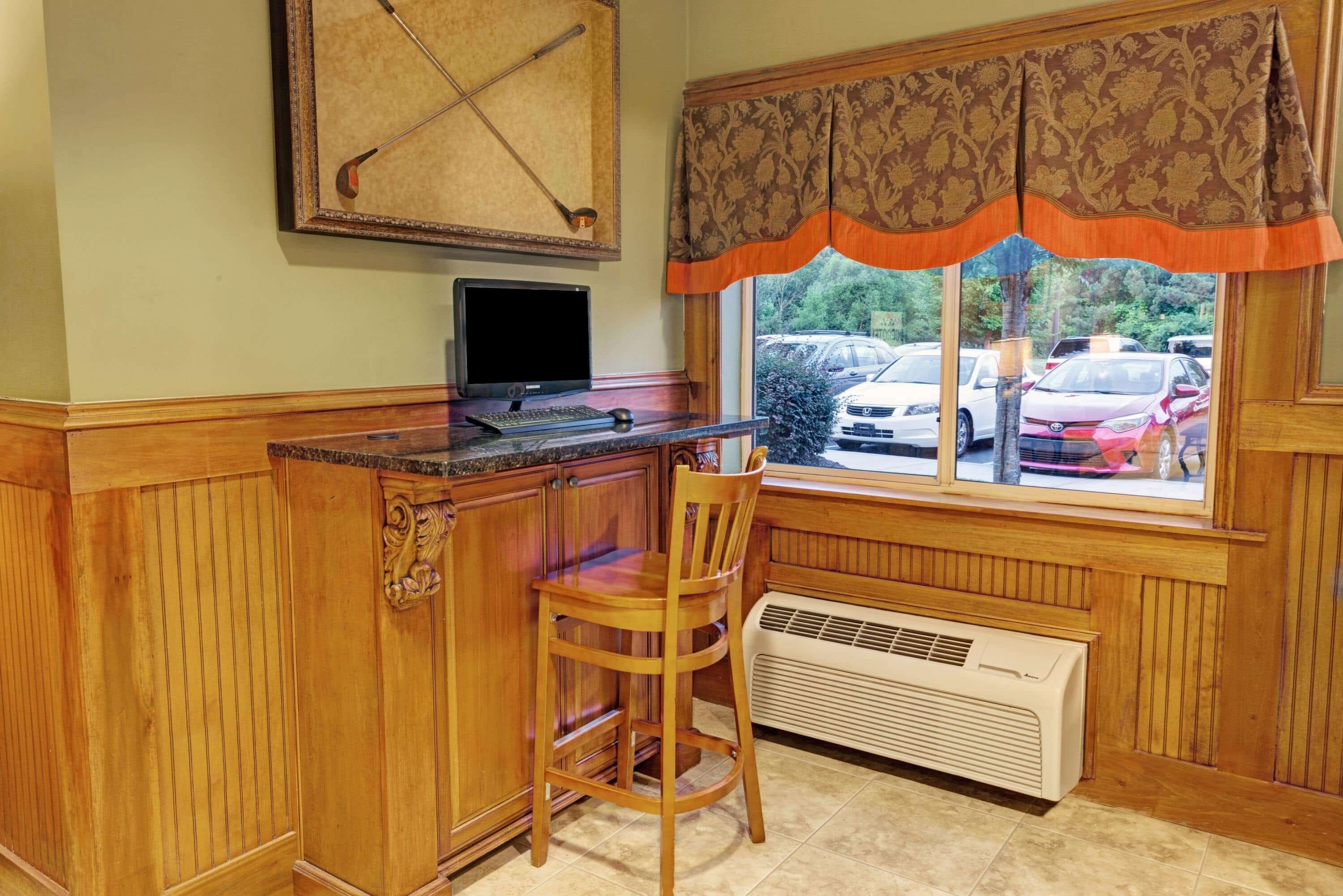 A kitchen with wooden cabinetry, a built-in stove, a window with patterned curtains, and a view of parked cars outside.