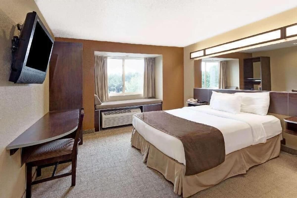 Une chambre d’hôtel comprenant un lit, un bureau, une chaise, une télévision, une fenêtre avec des rideaux et un miroir.
