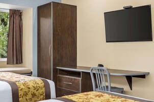 A hotel room with a bed, a desk with a chair, a wardrobe, and a flat-screen TV mounted on the wall.