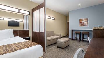 Ein Hotelzimmer mit Bett, Sofa, Hocker, Schreibtisch und Fernseher.
