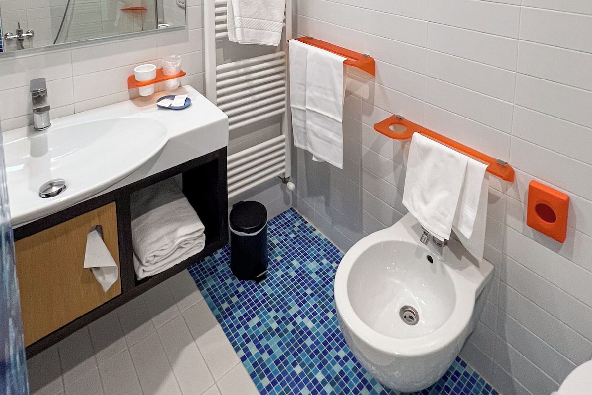 Um banheiro com pia branca, bidê, espelho, porta-toalhas e piso revestido de azulejos azuis.