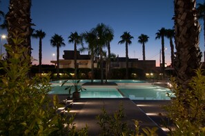 A swimming pool area at dusk with palm trees and a building in the background. - Sanlu Hotel (Carpignano Salentino)