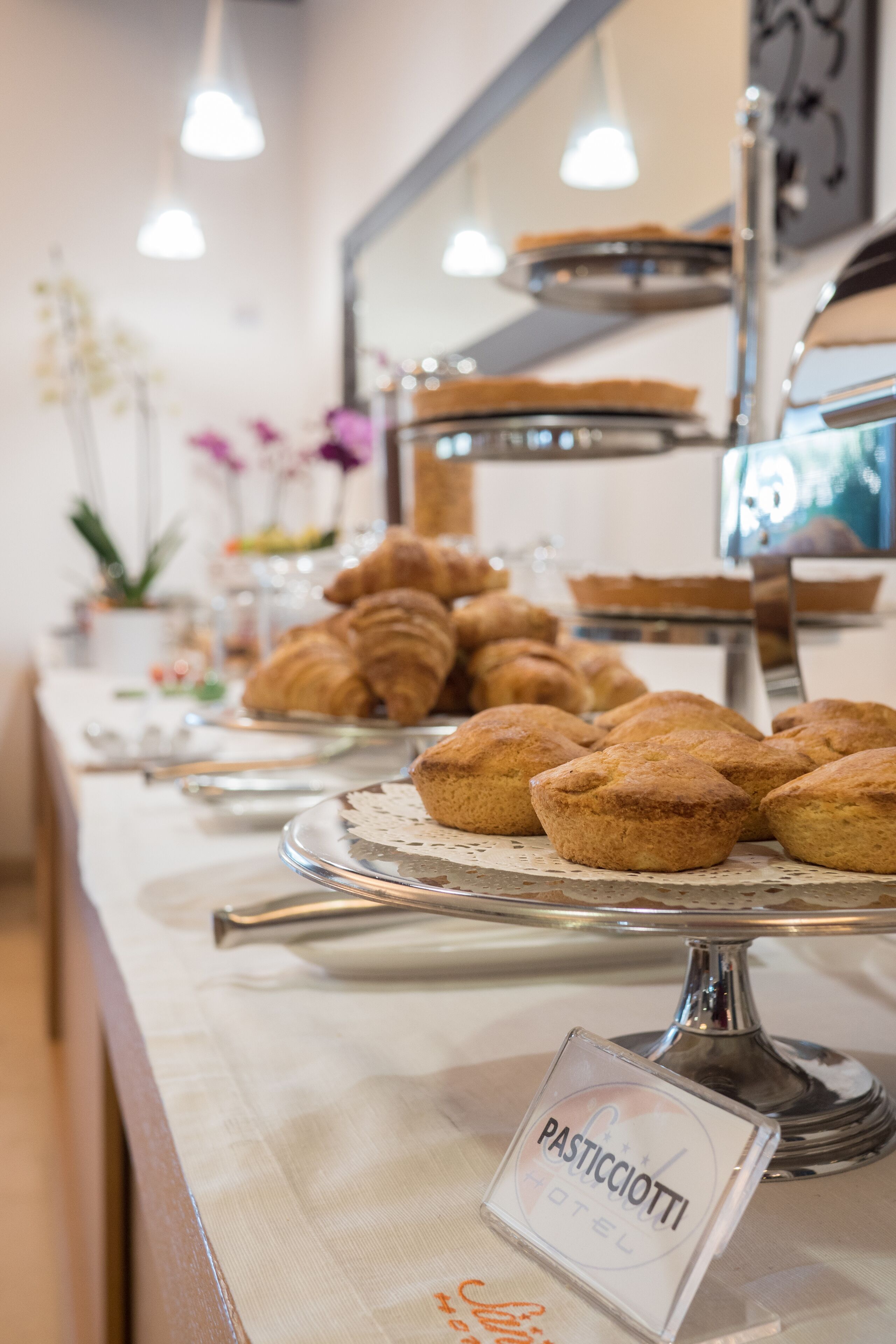 Een buffettafel met gebak en een bordje met de tekst 'PASTICCIIOTTI HOTEL'.