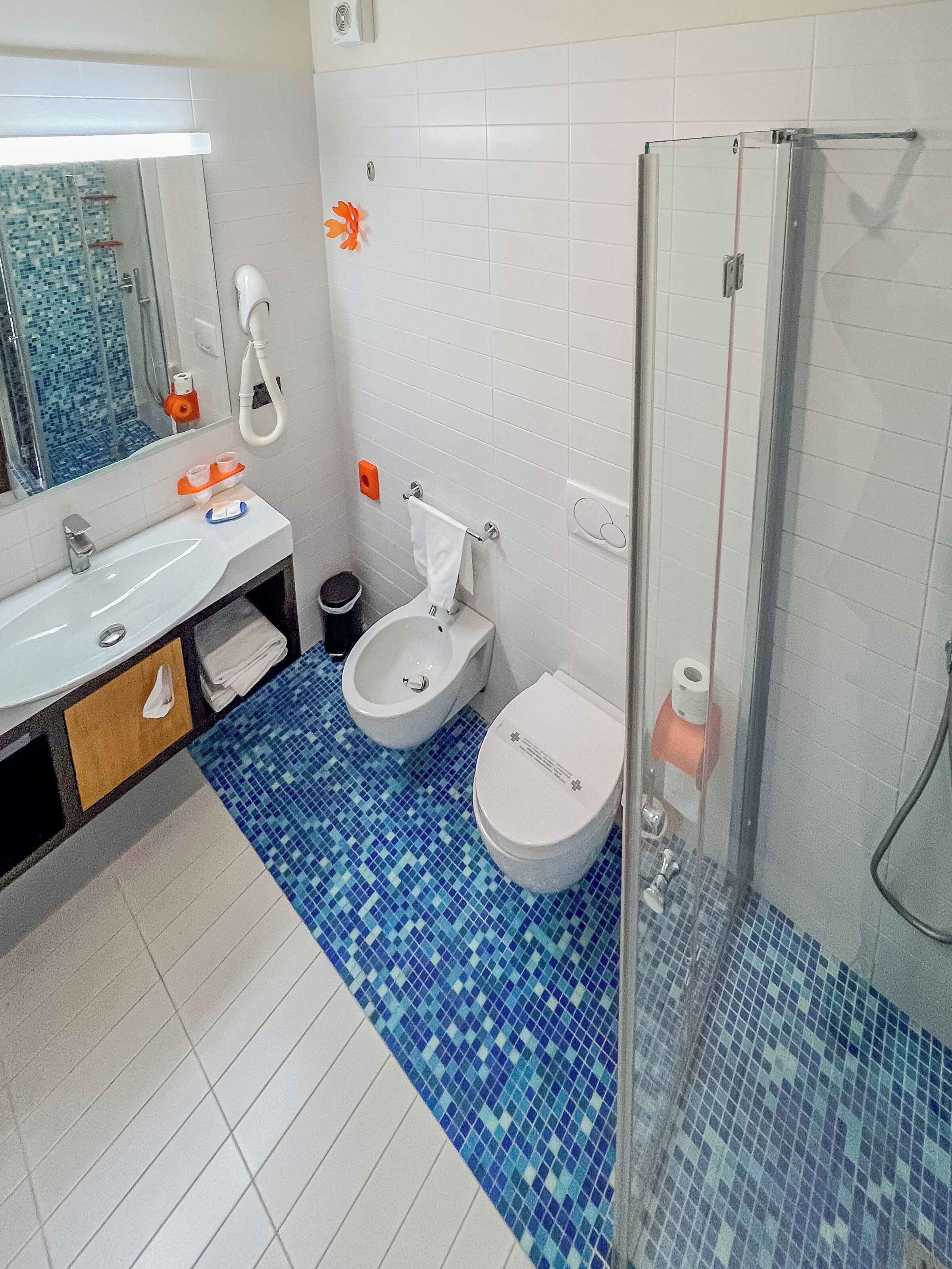 A bathroom with a white sink, two toilets, a shower, and a tiled floor.