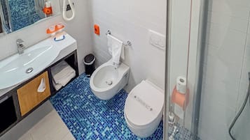 A bathroom with a white sink, two toilets, a shower, and a tiled floor.