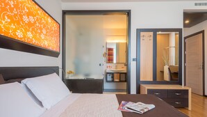 A modern hotel room with a large bed, a bedside table with a magazine, a bathroom visible through an open door, and a large mirror. - Sanlu Hotel (Carpignano Salentino)