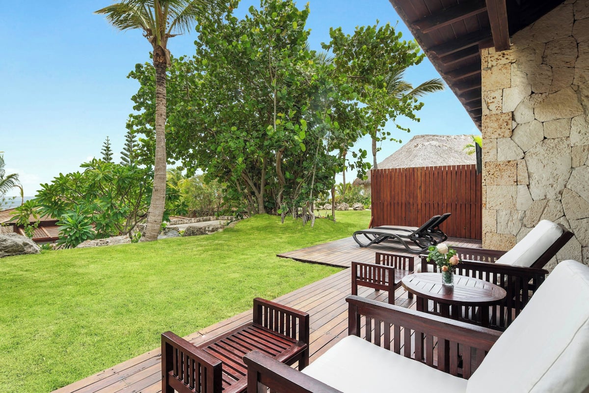A wooden deck with outdoor furniture, a stone wall, and a large tree.