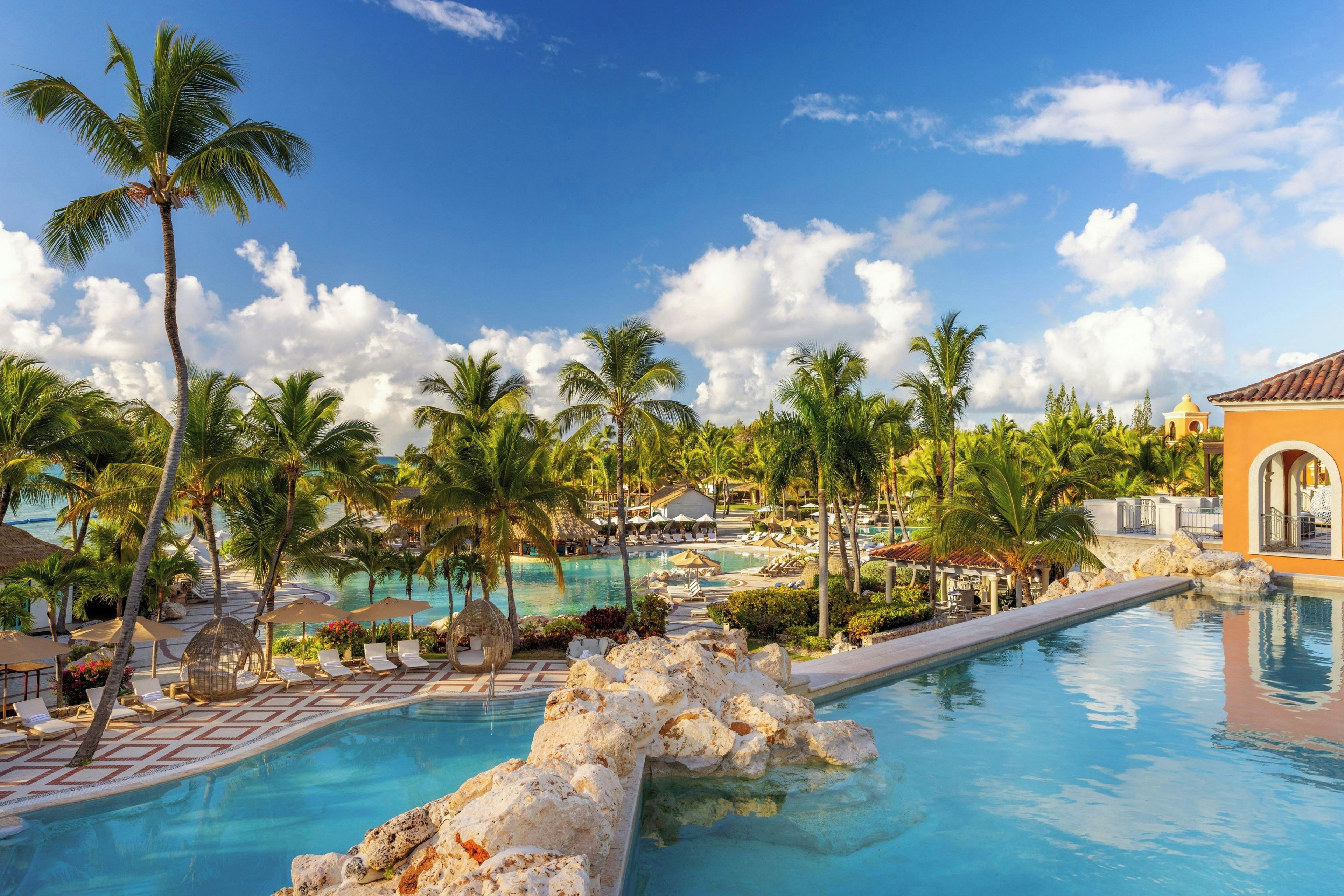 A resort pool area with palm trees, lounge chairs, and a clear blue sky.