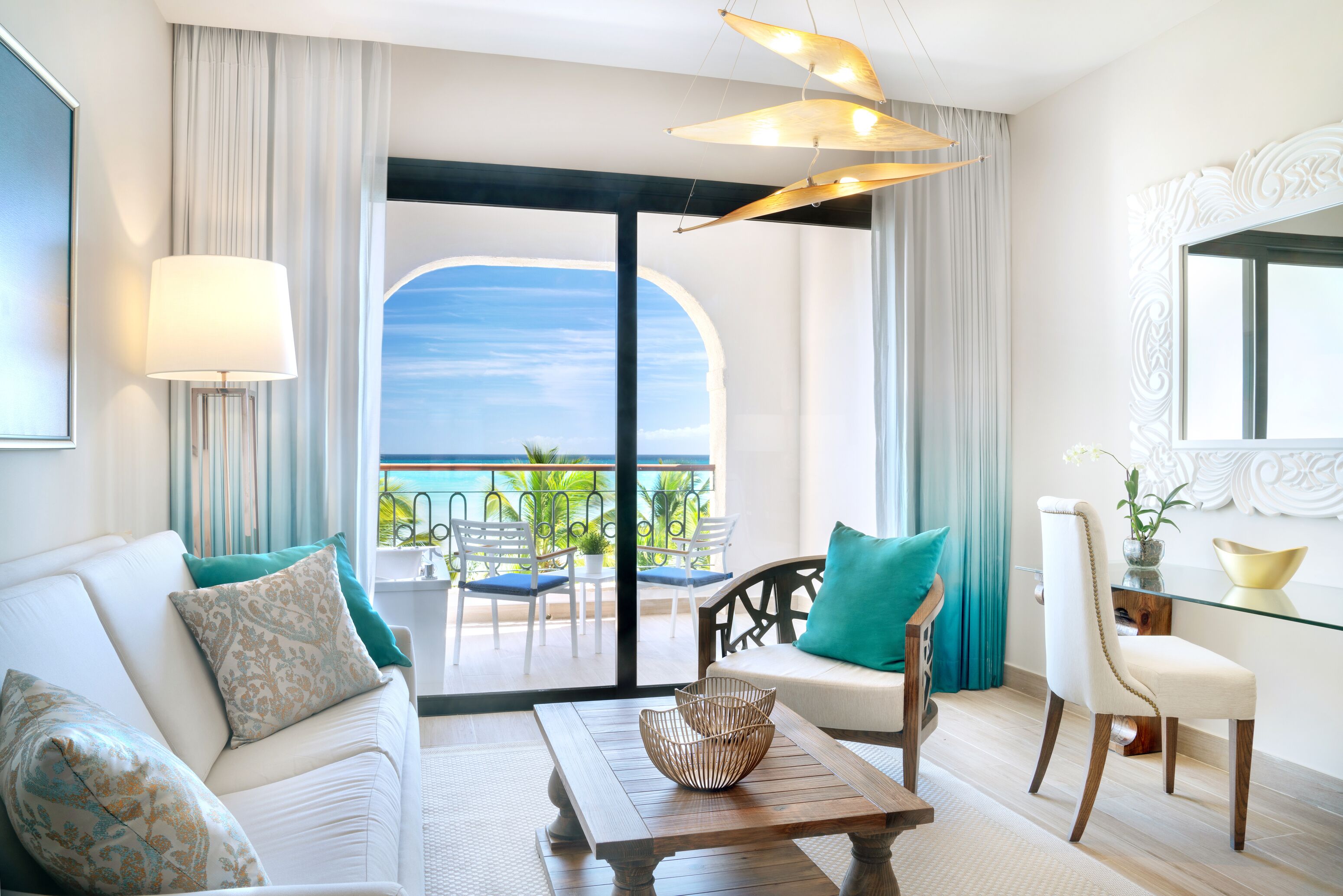 Een moderne hotelkamer met een bank, een eettafel en een stoel. Er is een balkon met uitzicht op de oceaan.
