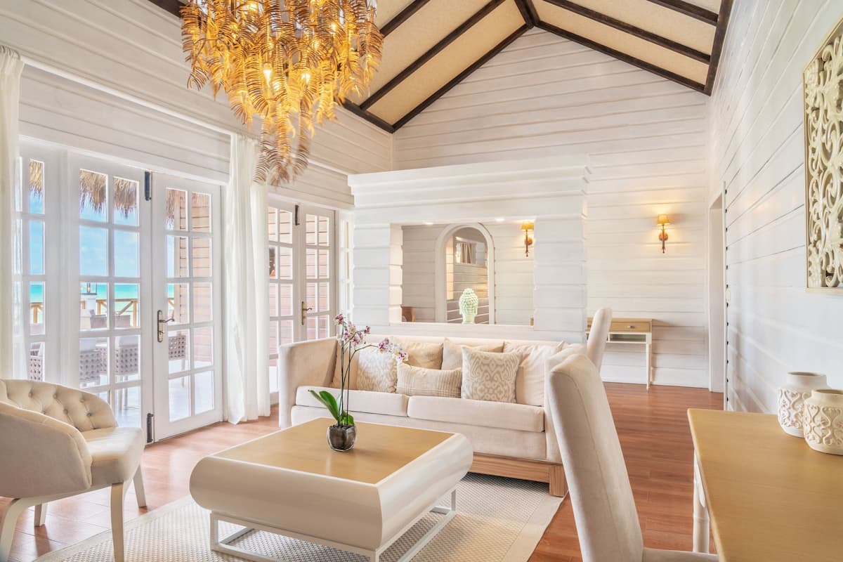 A spacious living room with a high ceiling, a large chandelier, and a view through glass doors to the outside.