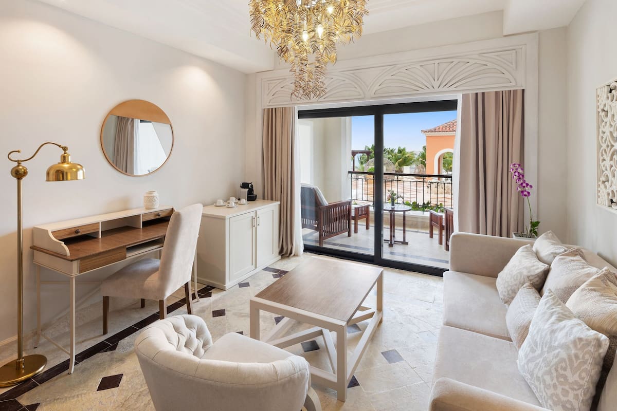 A modern hotel room with a desk, chair, sofa, and a view of the outdoor balcony.