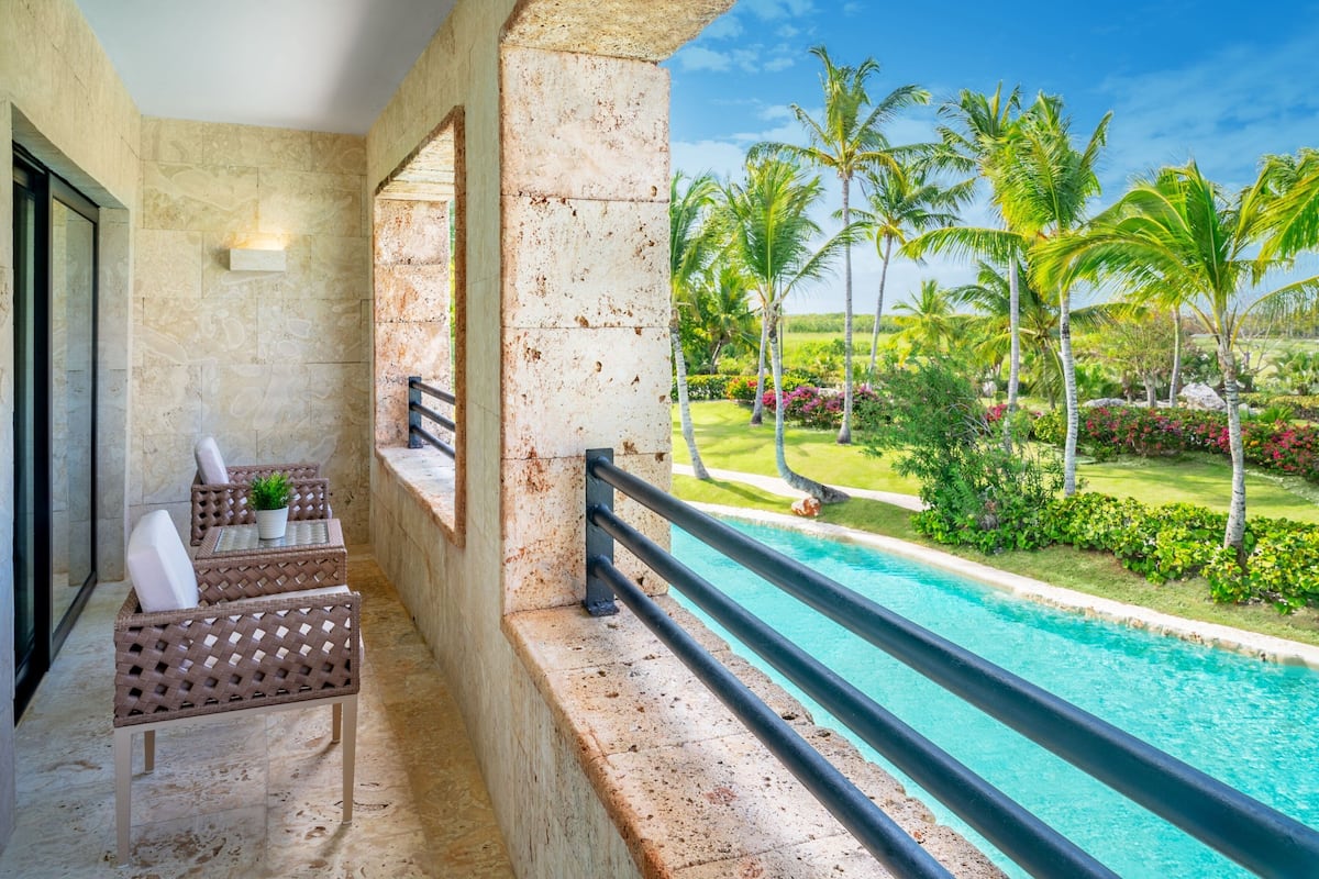 A balcony with a pool, wicker furniture, and a view of a tropical garden.