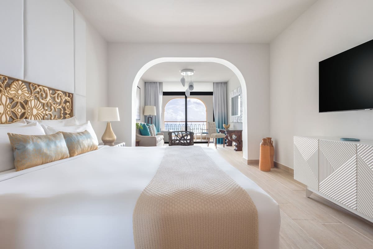 A modern hotel room with a large bed, a TV, a balcony with a view, and a dining area.