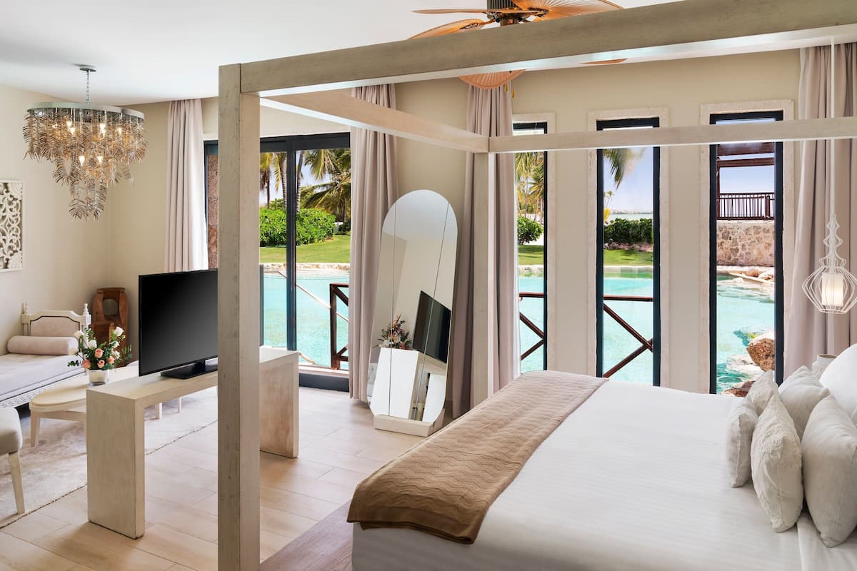 A spacious bedroom with a large bed, a TV, and a view of a pool.
