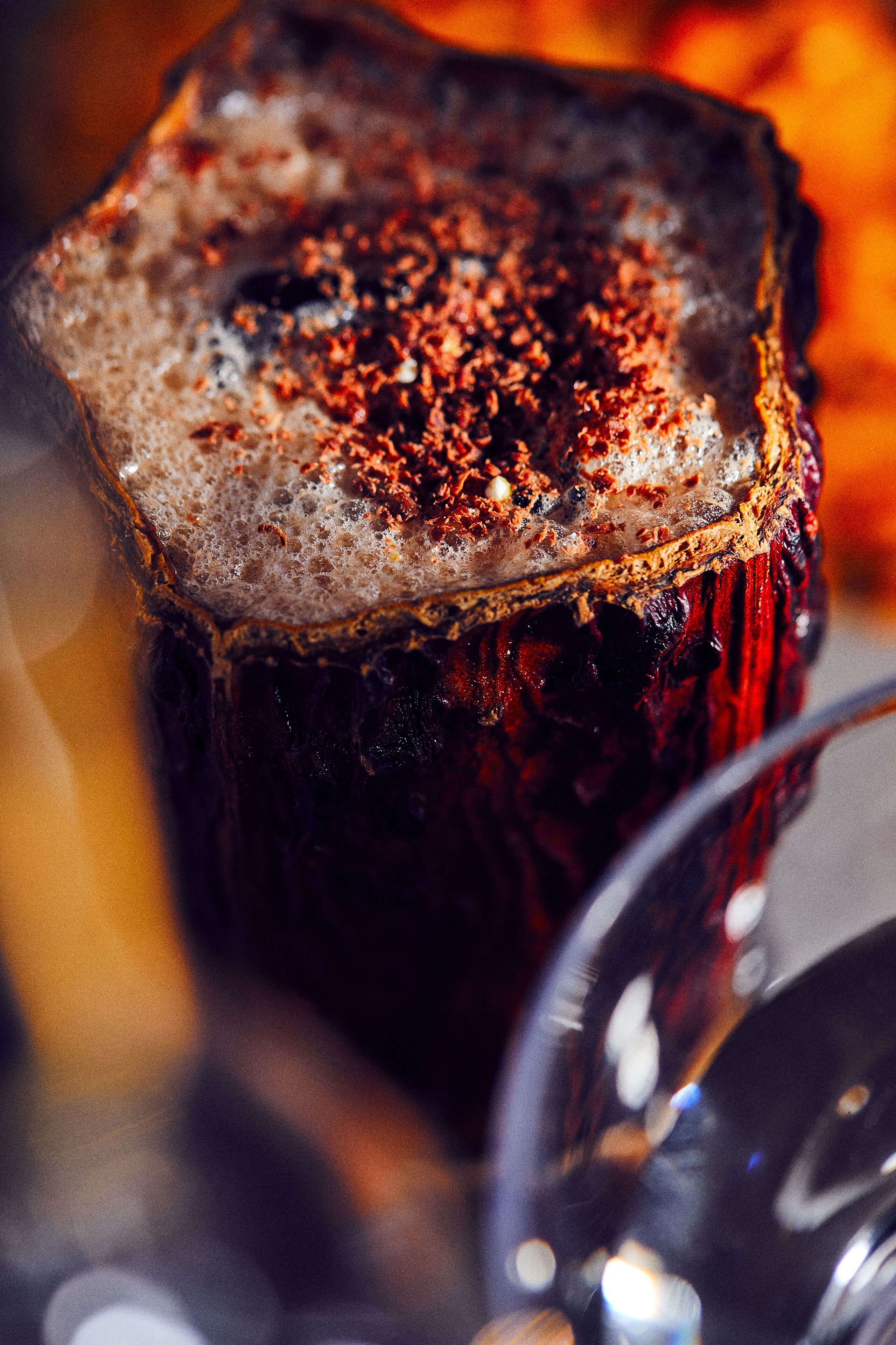 A close-up of a dark-colored beverage with a frothy top, possibly a cocktail or a hot drink, in a glass.