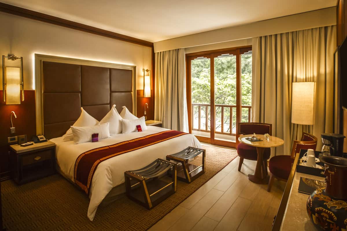 A hotel room with a large bed, a desk with a chair, a TV, and a window with curtains.