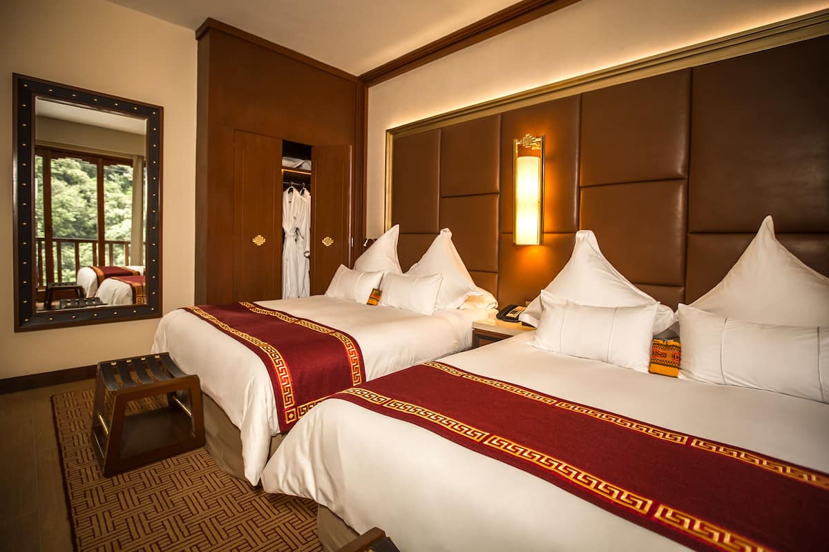 A hotel room with two beds, a large mirror, and a bedside table.