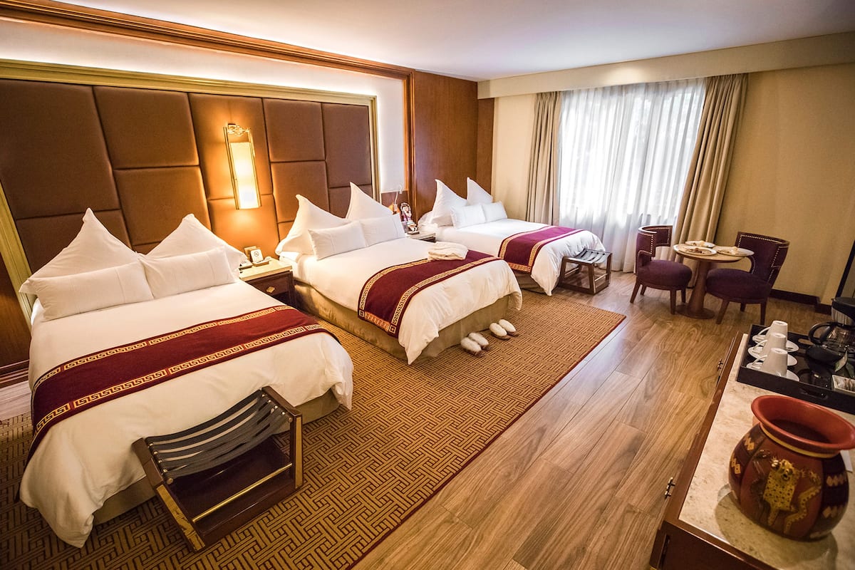 A hotel room with two beds, a desk, a chair, a small table, and a decorative vase.