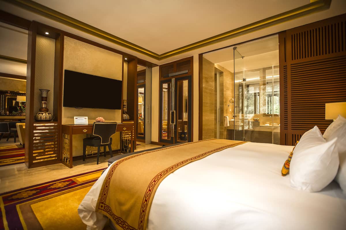 A hotel room with a large bed, a desk with a computer, a television, and a bathroom with a glass shower.