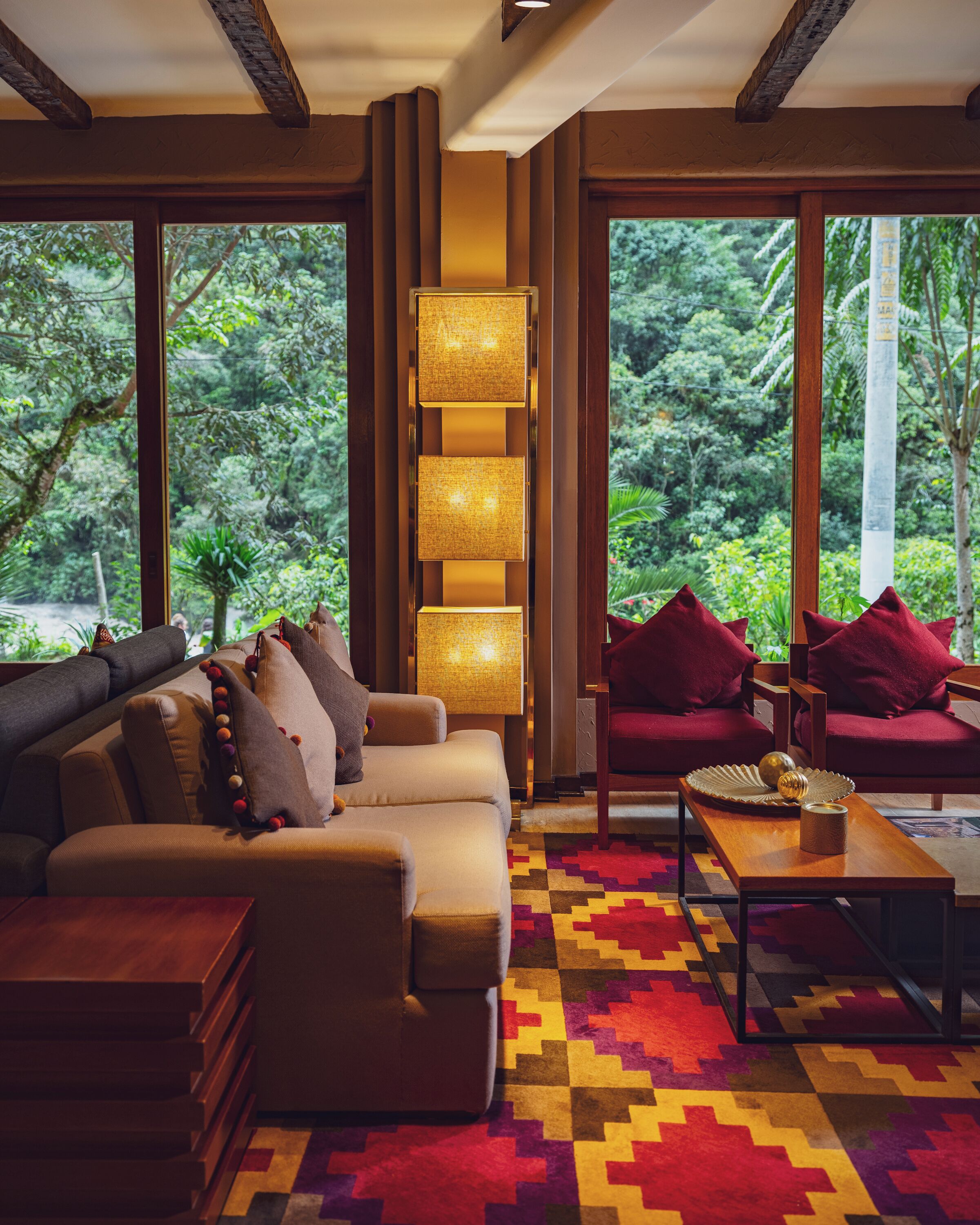 Una sala moderna con sofá, sillones, una mesita de centro y una lámpara de pie alta. Amplias ventanas ofrecen vistas a exuberante vegetación.