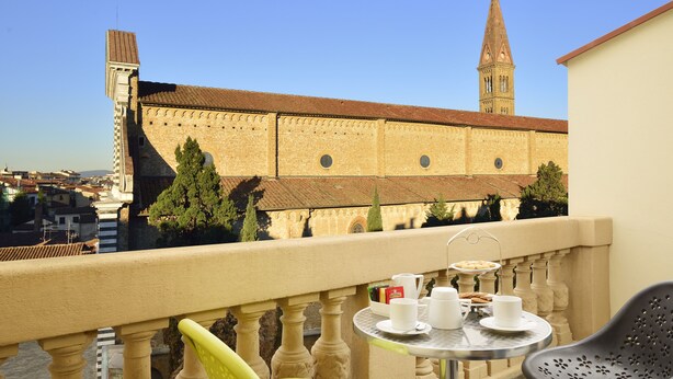 Un balcón con una mesa dispuesta para dos personas, con vista a un edificio histórico y una torre alta.