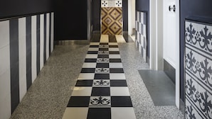 Un pasillo con piso a cuadros blanco y negro, puertas blancas y una pared de azulejos con diseño.