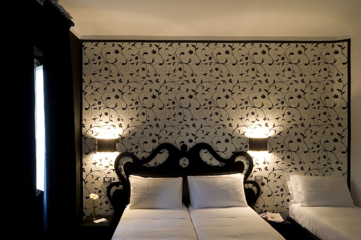 A double bed with a dark headboard, two bedside lamps, and a floral wallpaper pattern.