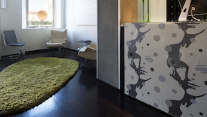 Un área de recepción moderna con un mostrador, sillas, una alfombra verde y una pared con un diseño original.