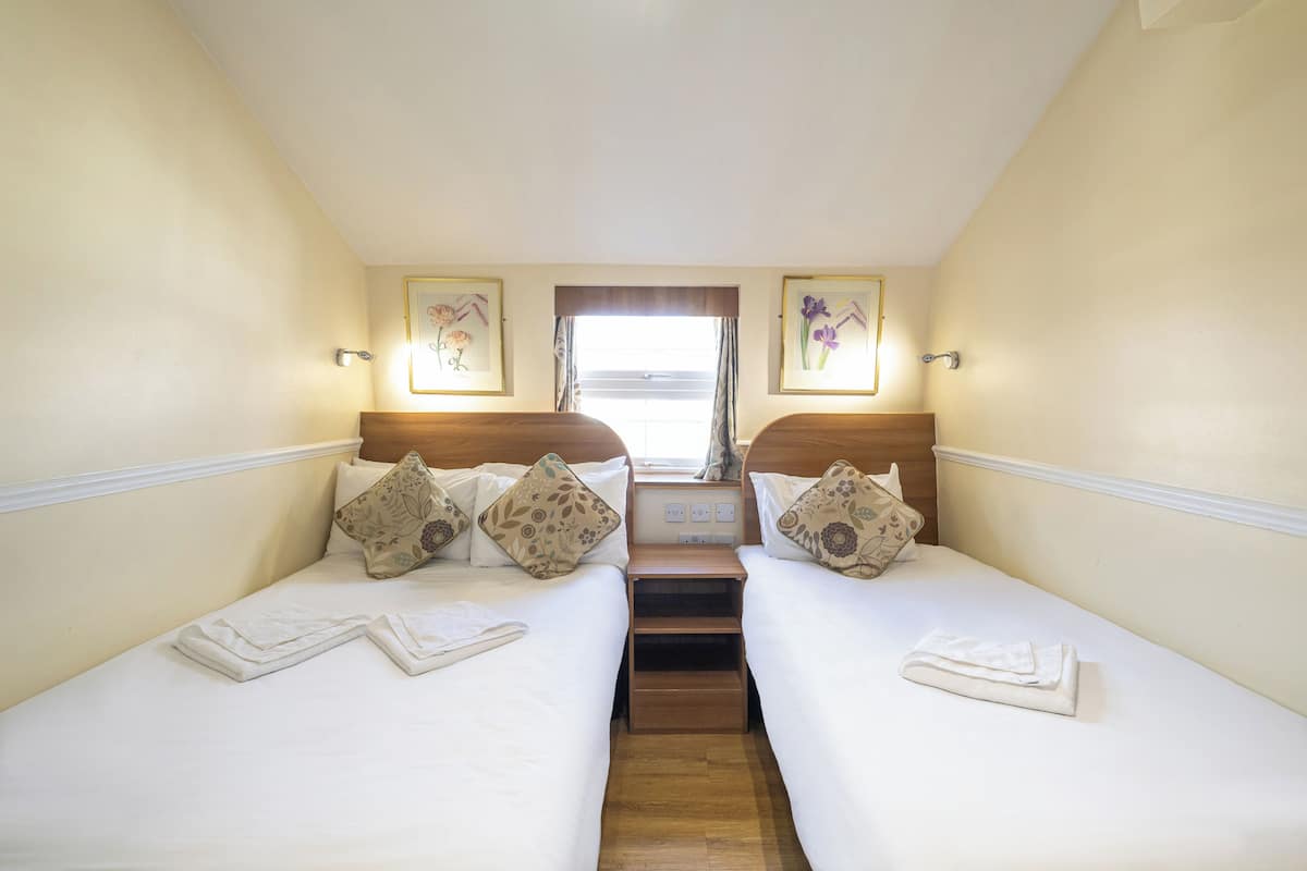 A twin room with two beds, a small window, and a nightstand between them.
