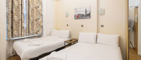 A hotel room with two beds, a window with curtains, a painting on the wall, and a small table.