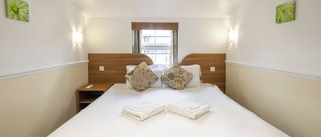 A hotel room with a large bed, two bedside tables, a window with curtains, and wall-mounted lights.