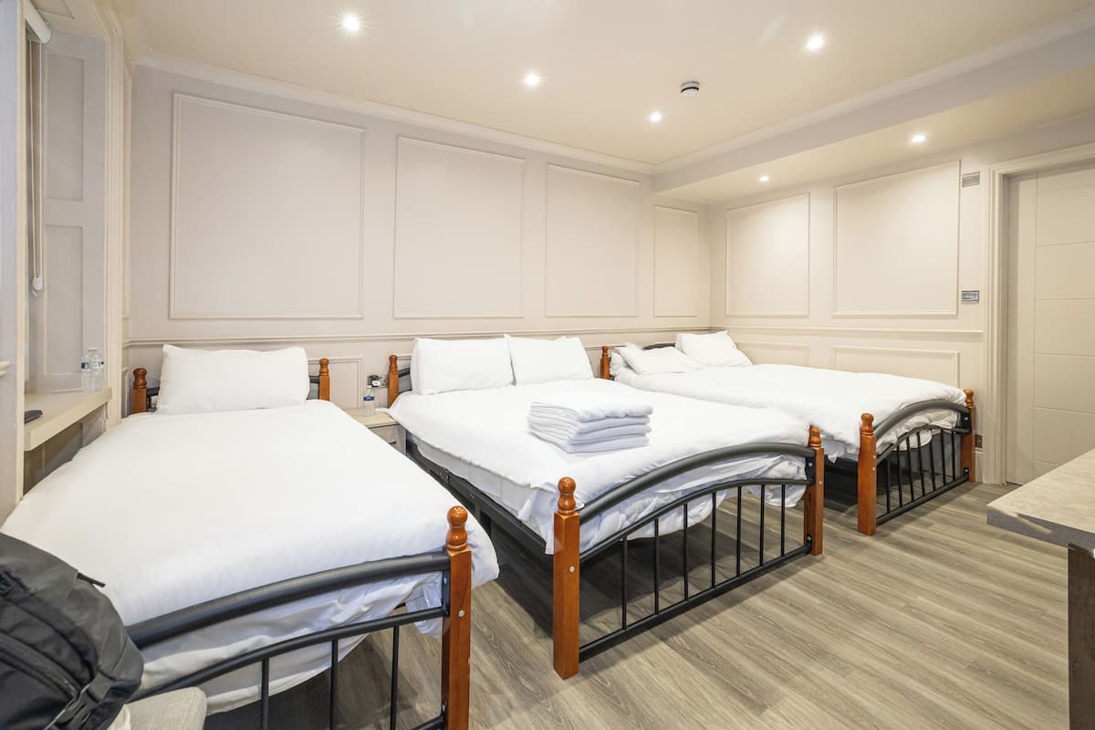 A hotel room with three beds, a wooden floor, and white walls.