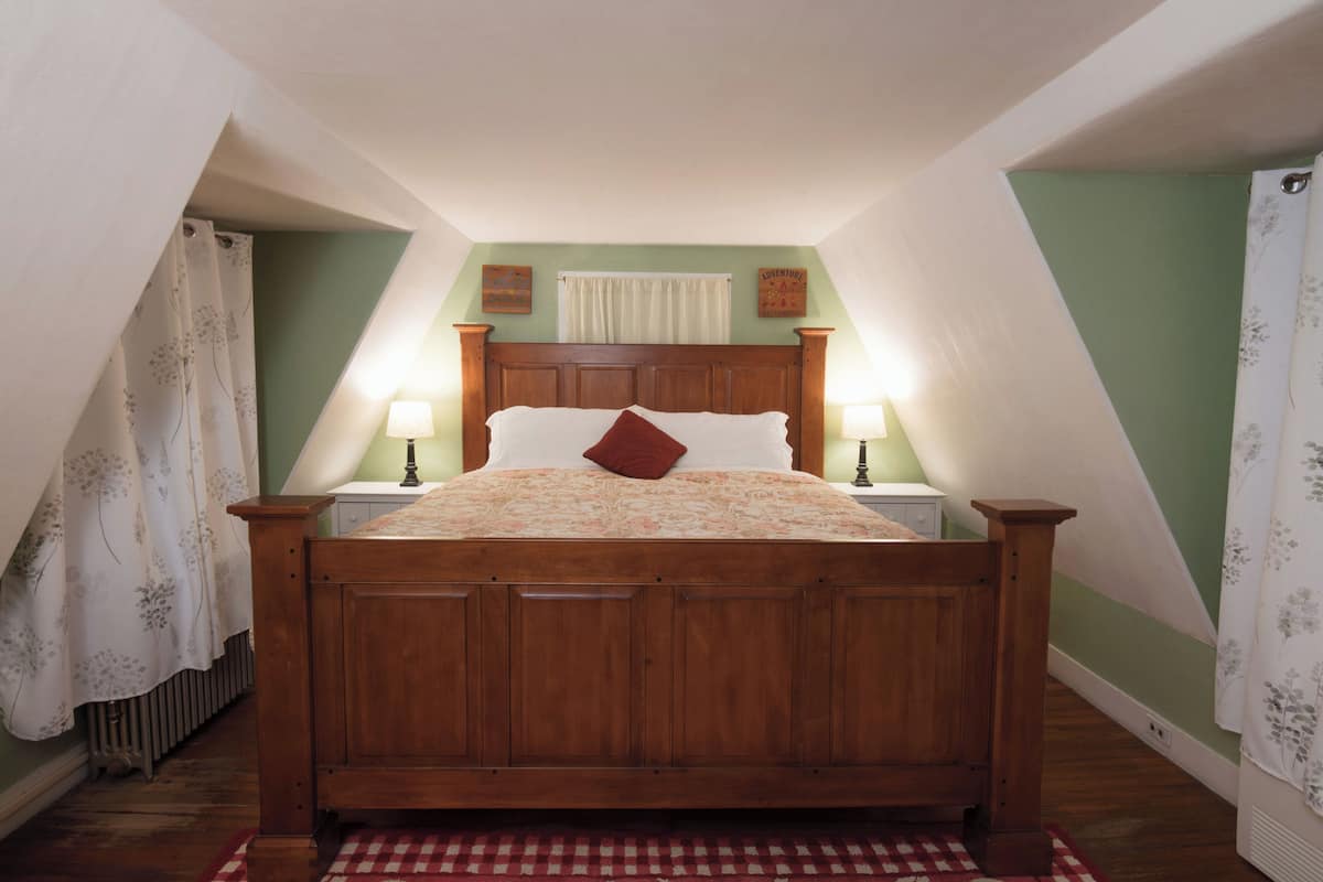 A bedroom with a wooden bed, two bedside lamps, a red pillow, and a checkered rug.