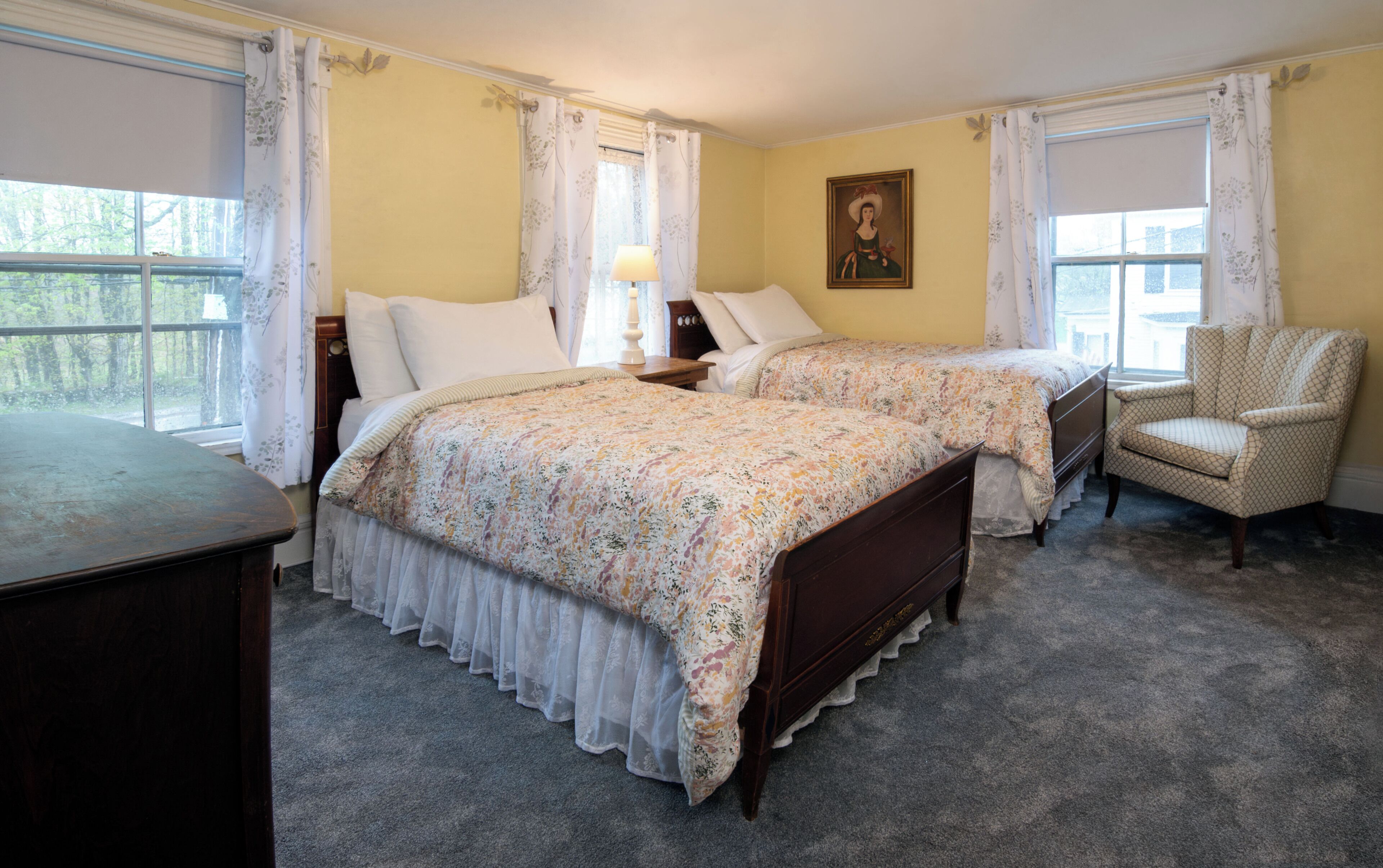 A bedroom with two beds, a chair, a dresser, and a painting on the wall.
