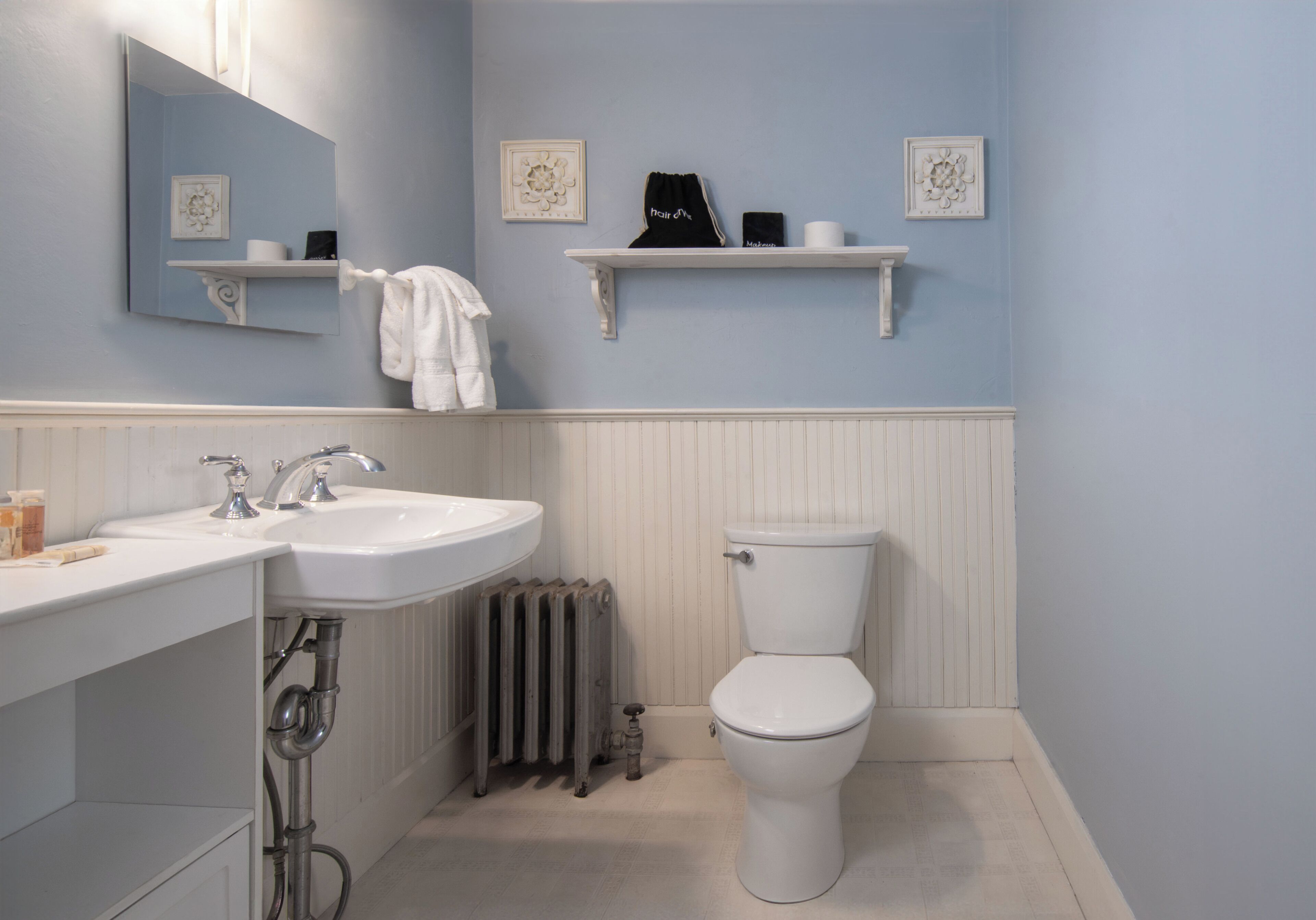 Ein Badezimmer mit einem weißen Waschbecken, einer Toilette und einem Spiegel. Zwei Handtuchhalter mit aufgehängten Handtüchern.