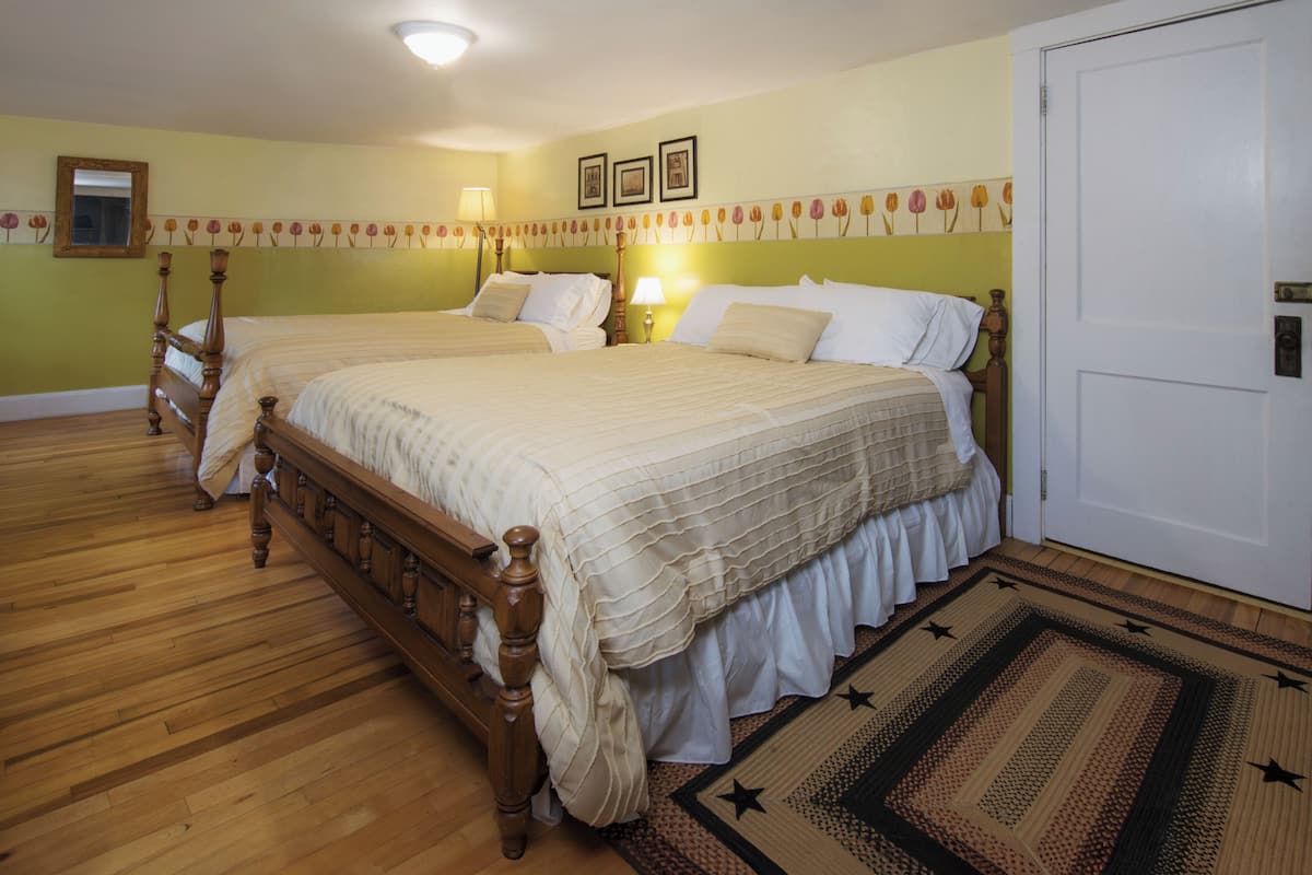 A double bed with a wooden frame and white bedding, a wooden floor, and a door to the right.