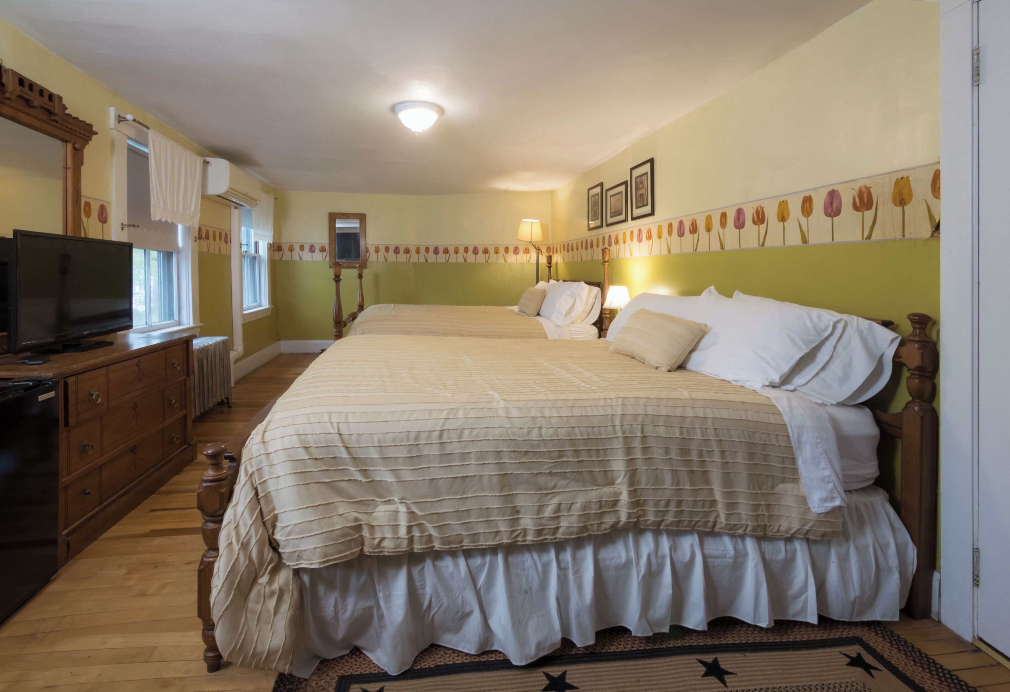 A bedroom with a large bed, a dresser, a television, and a window with curtains.
